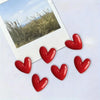 A set of red heart-shaped fridge magnets placed on a white surface next to a photo of dry grass.