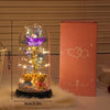 A glass dome containing a glowing purple rose and golden foliage, displayed next to its pink box.