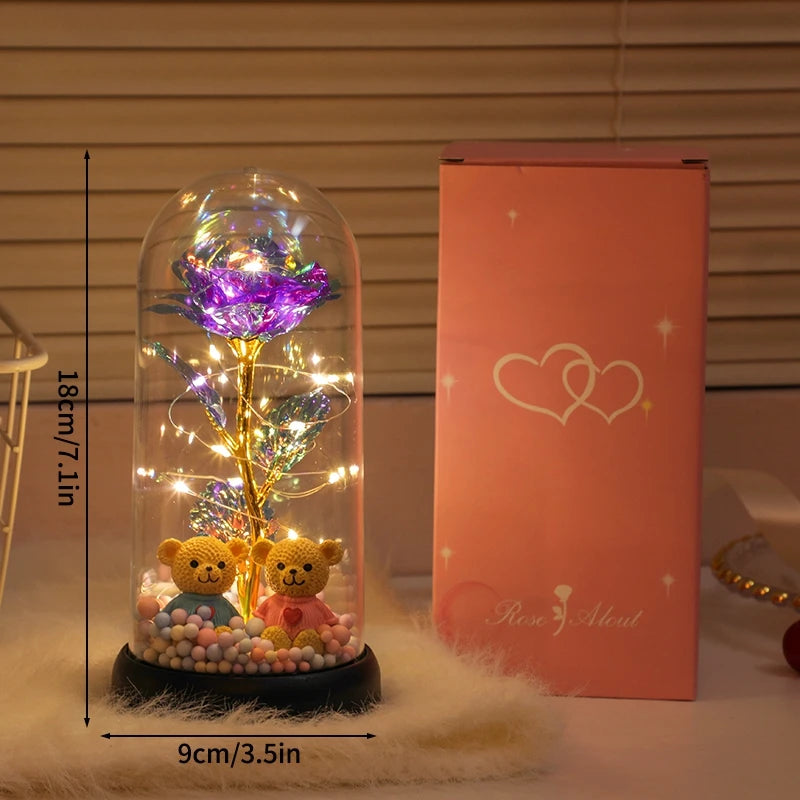 A glass dome containing a glowing purple rose and golden foliage, displayed next to its pink box.