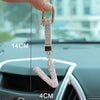 A close-up of a crystal letter keychain charm, shaped like the letter I, being held by a hand against a car interior backgrou
