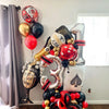 A cluster of gold, black, and red foil balloons shaped like dice decorating a party backdrop.
