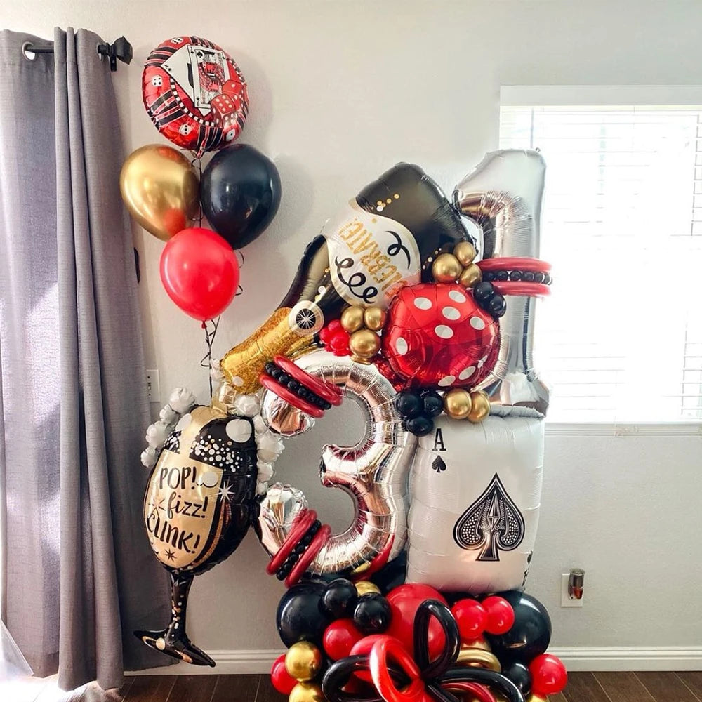 A cluster of gold, black, and red foil balloons shaped like dice decorating a party backdrop.
