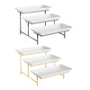 A set of three rectangular serving platter stands, two black and one gold, displayed against a white background.