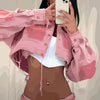Eine Frau mit dunklem Haar trägt eine rosa Jacke und ein helles Oberteil und macht ein Selfie mit einem weißen Smartphone.