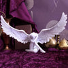 White resin angel wing figurine with a nude figure resting on a purple velvet fabric.