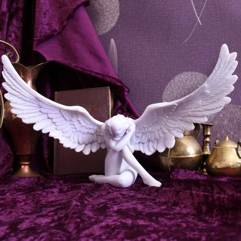 White resin angel wing figurine with a nude figure resting on a purple velvet fabric.