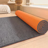 Orange cylindrical artificial grass carpet rolled out on a wooden floor.