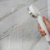 A hand holds a white spray bottle, spraying water onto a marble wall surface.