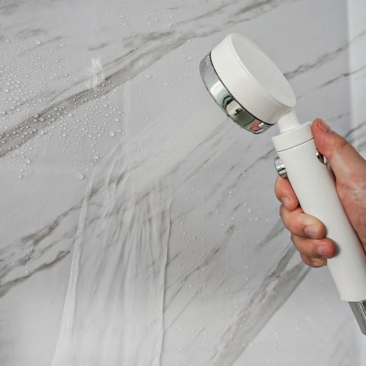 A hand holds a white spray bottle, spraying water onto a marble wall surface.