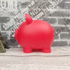 A bright red piggy bank shaped like a pig sitting on a light wooden surface.