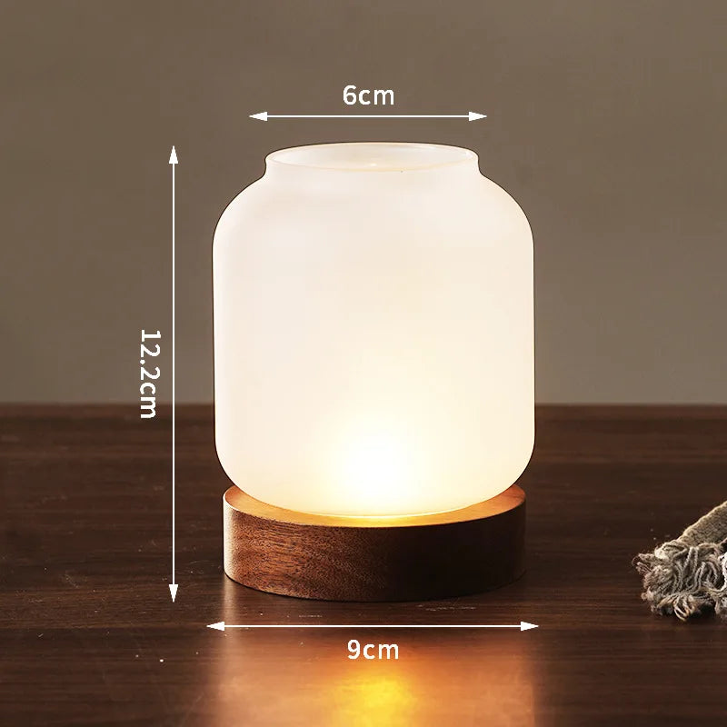 A white glass lantern with a wooden base and a warm glow, shown against a dark background.