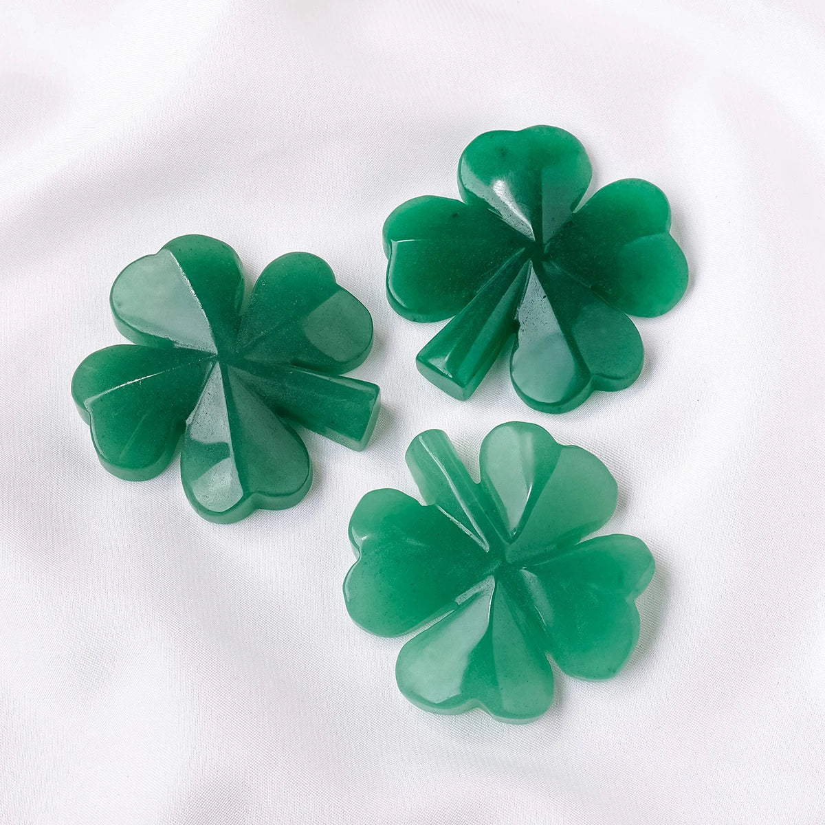 A cluster of green Aventurine quartz four-leaf clover crystal statues on a white background.