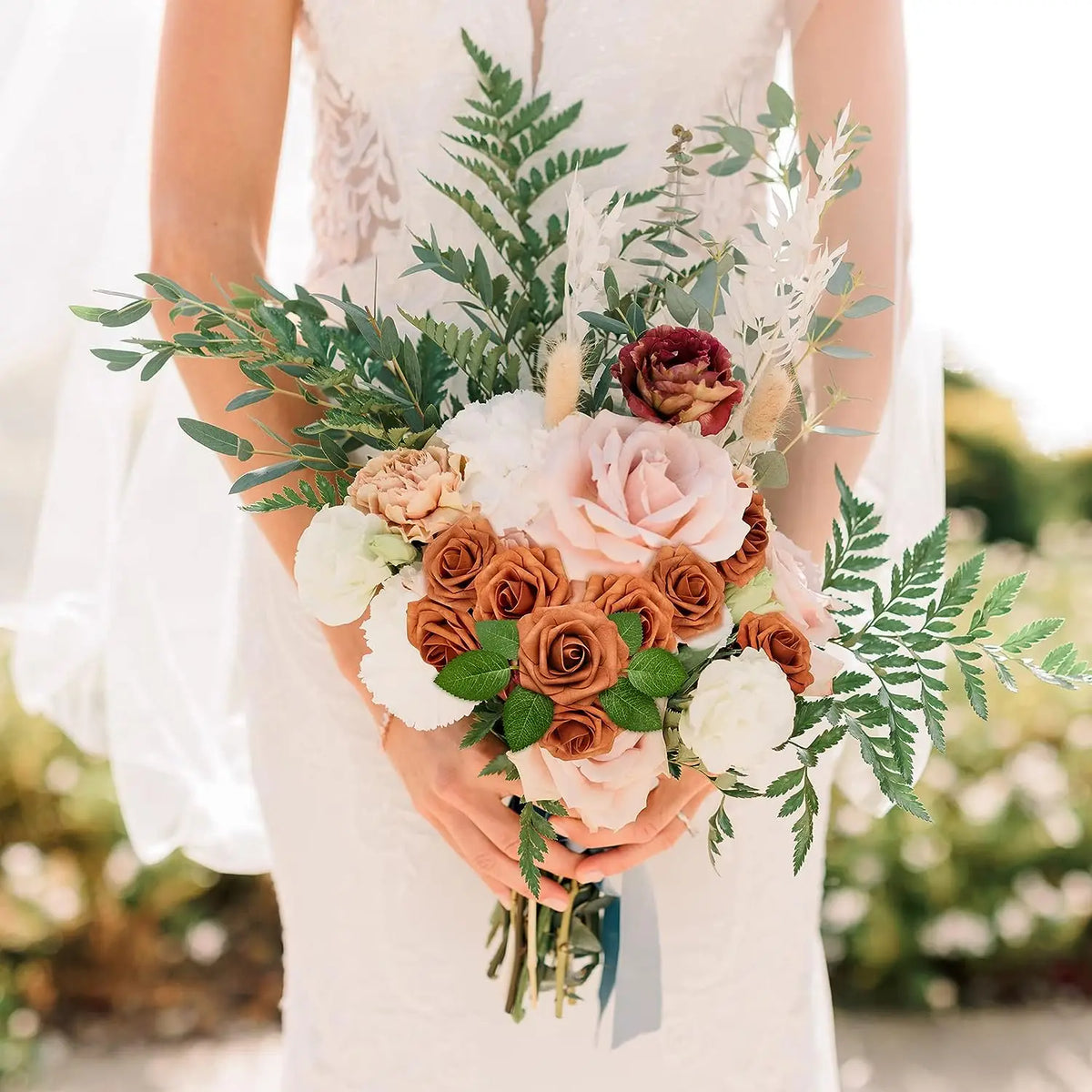 A bride holds a bouquet of artificial real touch foam roses and greenery in a wedding dress.