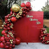 A large arrangement of deep burgundy latex balloons with gold accents, set against a red backdrop.