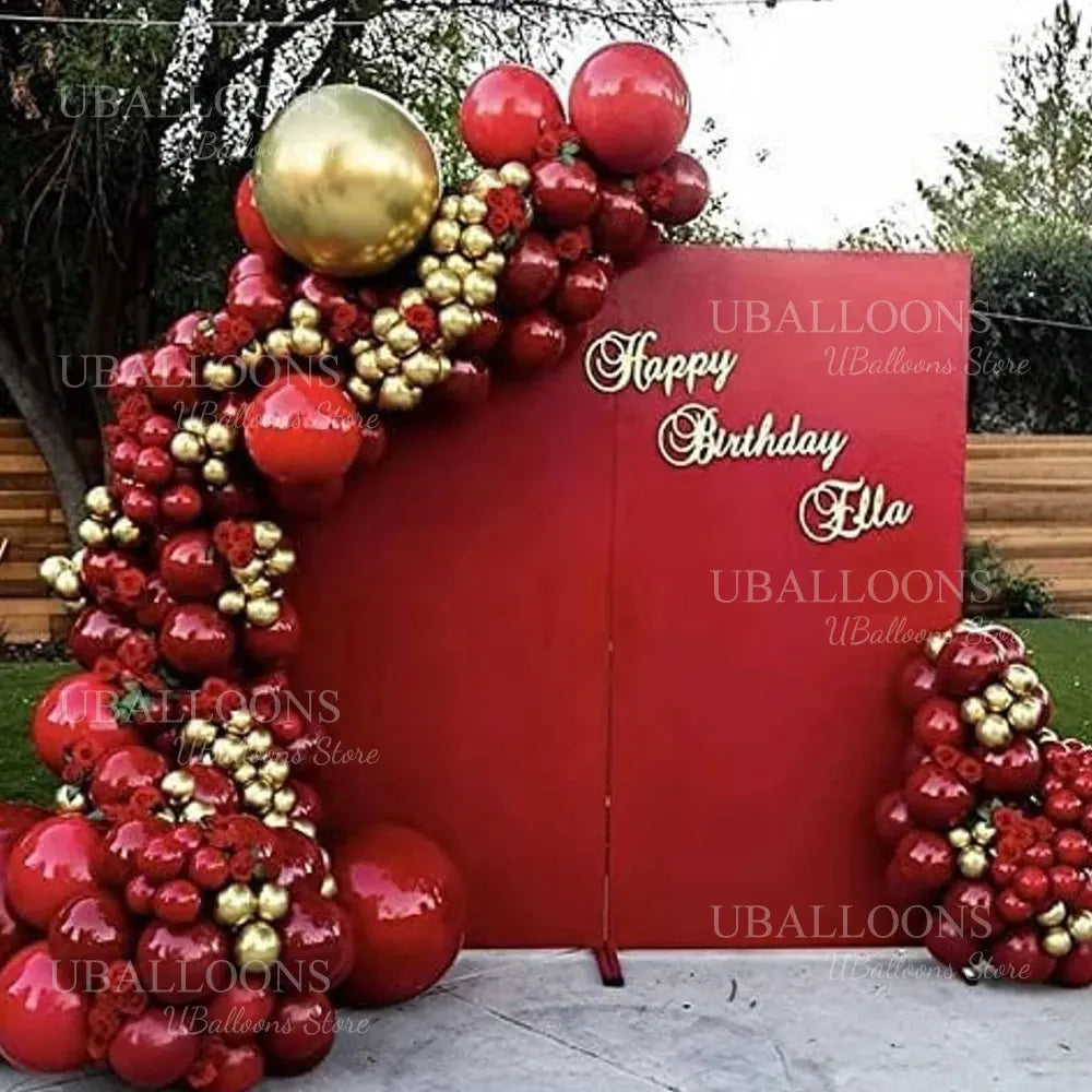 A large arrangement of deep burgundy latex balloons with gold accents, set against a red backdrop.