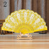 A yellow lace folding hand fan displayed on a wooden stand against a blurred background.