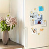A collection of gold heart fridge magnets displayed on a light-colored cabinet door next to a vase of pink flowers.
