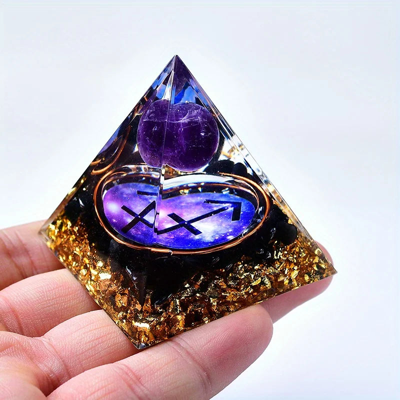 A hand holds a clear pyramid crystal with an amethyst decorative top and gold glitter base.