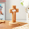 A handcrafted wooden cross standing ornament made of light-colored wood on a wooden surface.