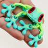 A hand holds a realistic, movable 3D printed frog fridge magnet with bright green and cyan accents.