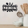 A black metal word sign spelling 'KITCHEN' with leafy accents, displayed on a white wall.