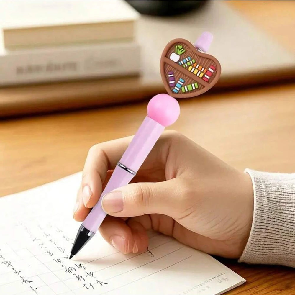 A hand holds a pink silicone pen writing on paper next to a wooden bead shaped like a syringe filled with colorful beads.