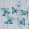 Several light blue and teal organza butterfly embellishments scattered on a white wooden surface.