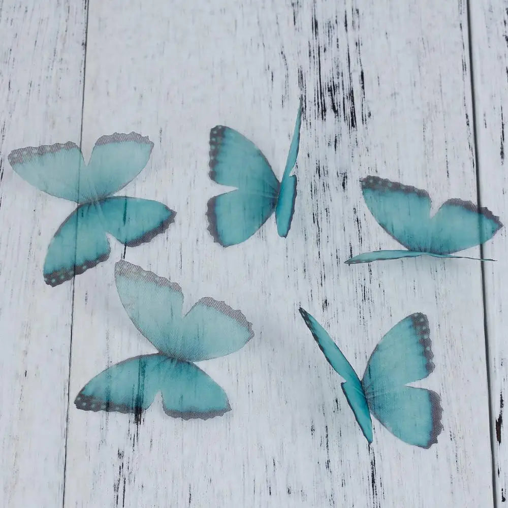 Several light blue and teal organza butterfly embellishments scattered on a white wooden surface.
