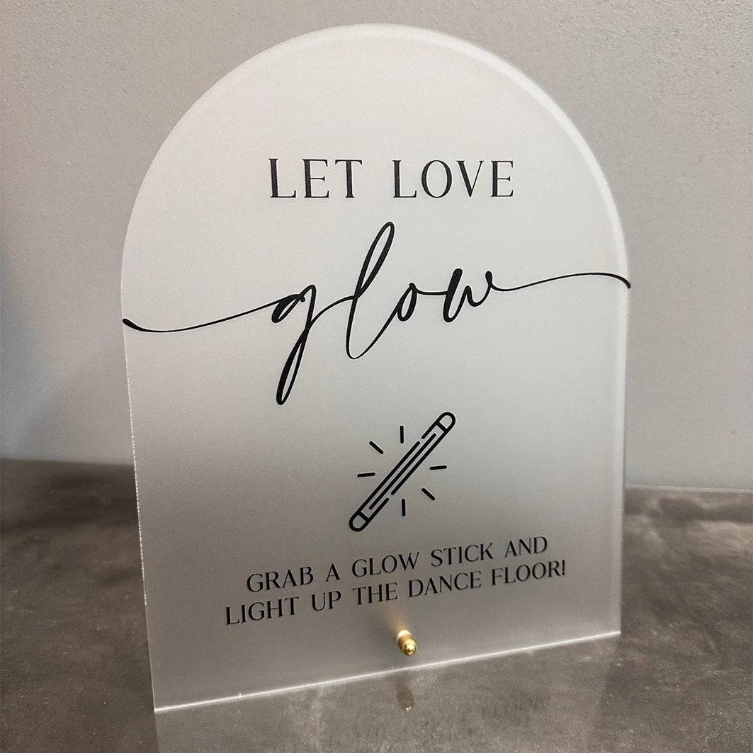 A clear acrylic sign with black script that reads Let Love glow and instructs to grab a glow stick and light up the dance flo