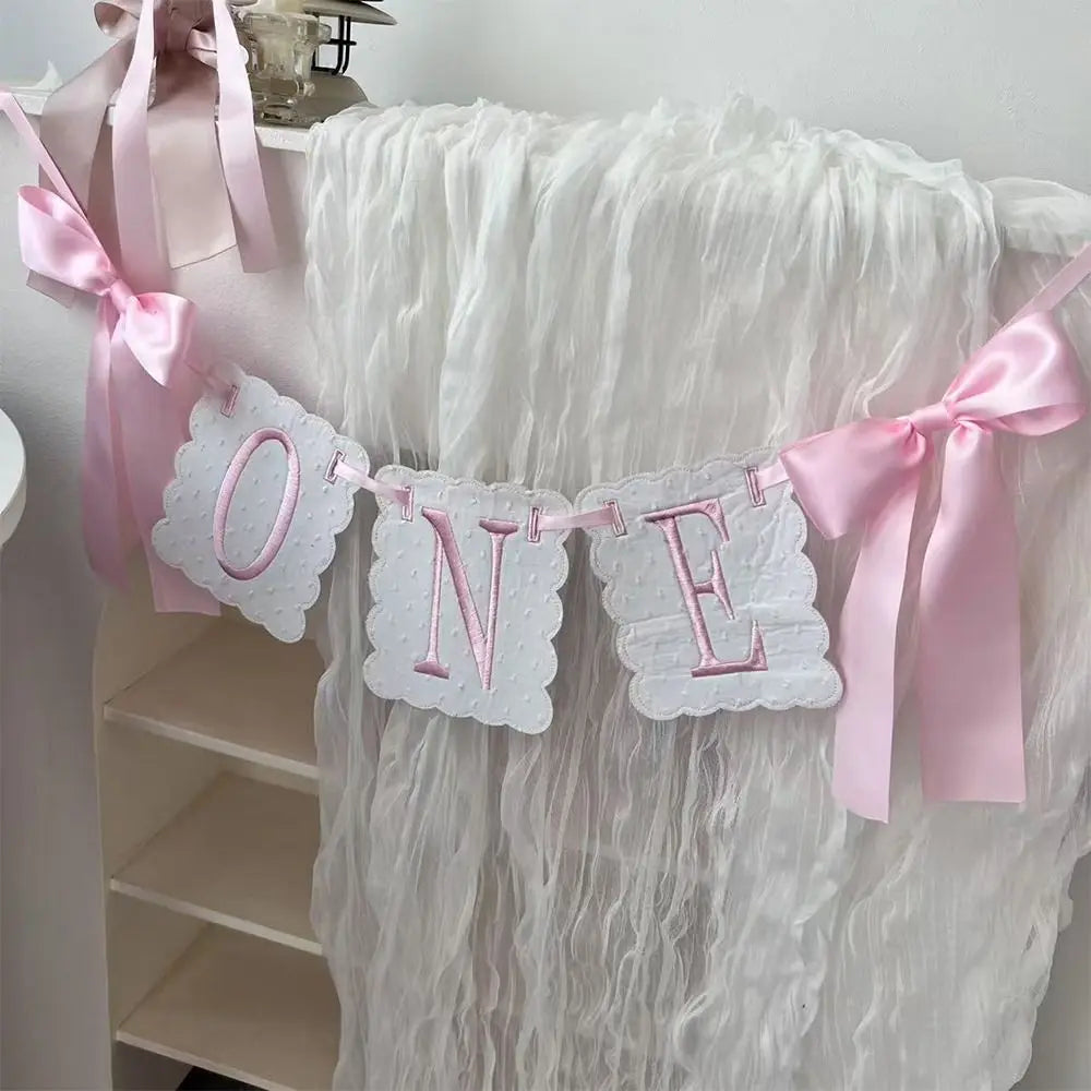 Pink ribbon garland with die-cut letters spelling ONE for a first birthday decoration