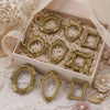 A set of vintage gold resin mini photo frames displayed in a light wooden box on white lace fabric.