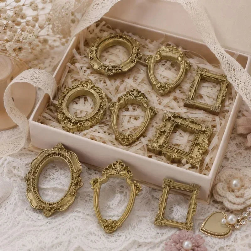 A set of vintage gold resin mini photo frames displayed in a light wooden box on white lace fabric.