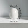 A white ceramic mini vase with a smooth, rounded shape is shown on a shelf.