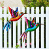 Vibrant metal hummingbird wall art featuring iridescent colors displayed against a white picket fence.