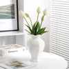 Elegant white ceramic vase with floral relief detailing holding green tulips on a white table.