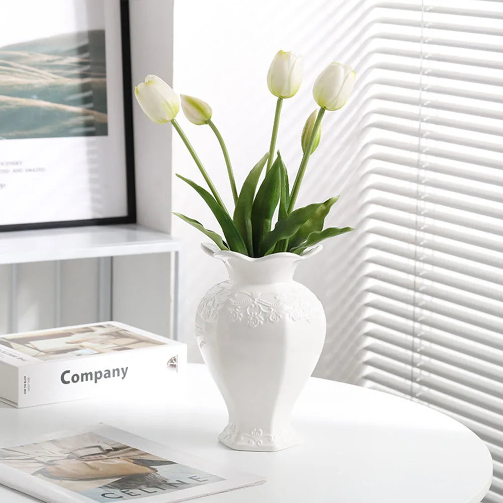 Elegant white ceramic vase with floral relief detailing holding green tulips on a white table.