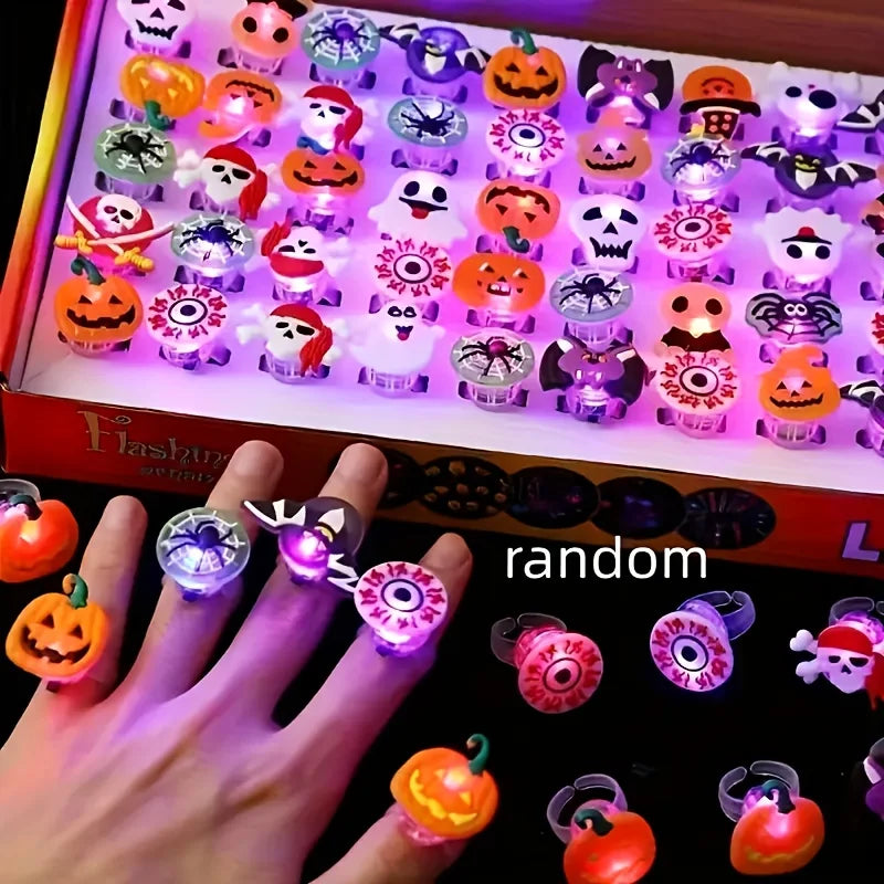 A hand displays a large box of Halloween glow rings set with various spooky and cute designs.
