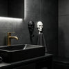 A black vessel sink is set against a dark gray tiled wall featuring two decorative skull wall hooks.
