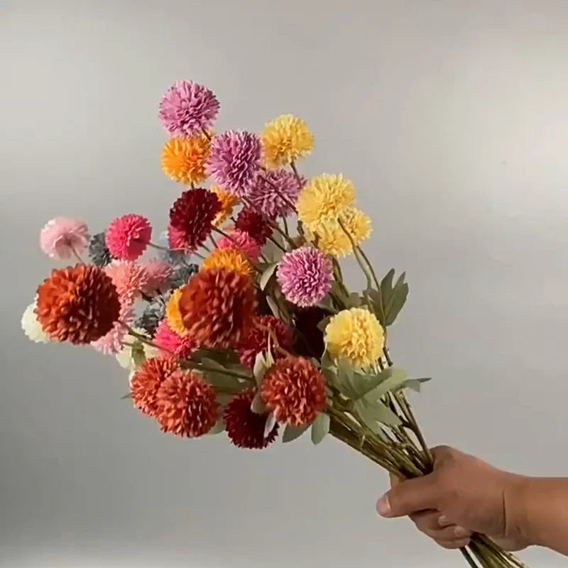 Un ramo de flores artificiales de crisantemo y diente de león en tonos rosa, naranja y amarillo.