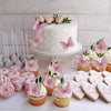 A display of pink butterfly cupcake toppers and cupcakes arranged on a white surface.