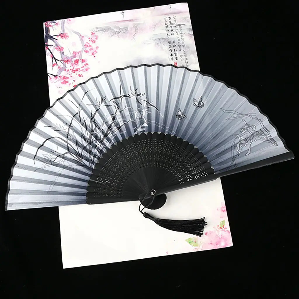 A vintage silk folding fan with gray and black stripes and delicate Oriental patterns is displayed on white paper.