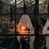 A glowing orange pumpkin sits behind a sheer black gauze fabric decoration in a dark, spooky setting.