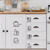 White kitchen cabinet doors featuring black line drawings of various cooking utensils and tableware.