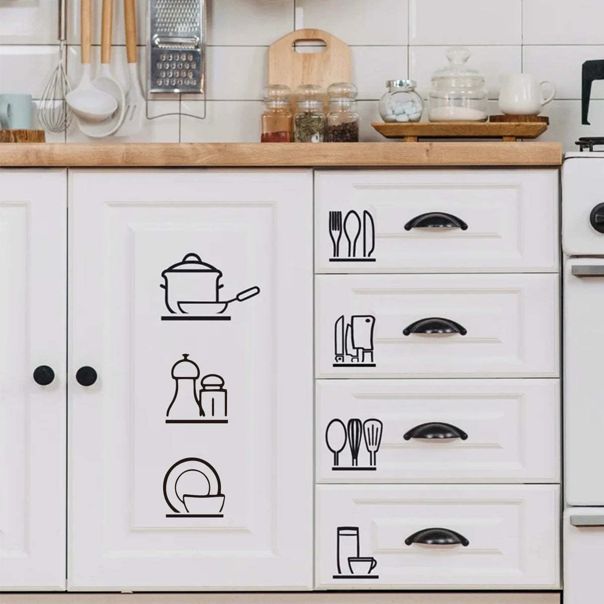 A set of black line art stickers depicting various kitchen utensils and cookware on a white cabinet door.