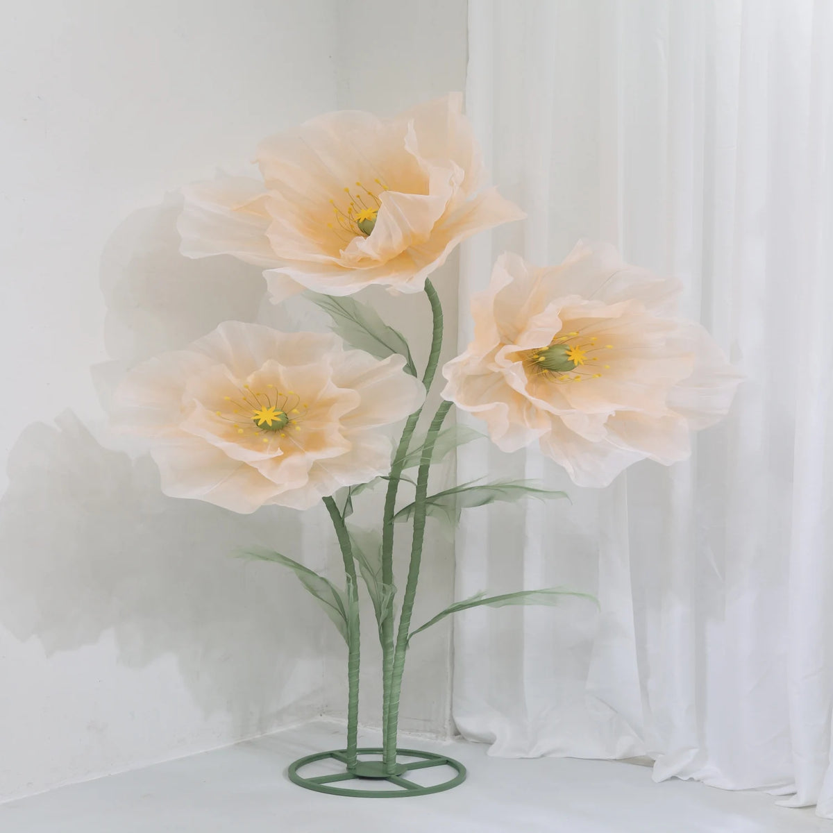 Large artificial silk peach colored poppy flower displayed on a green stand against a white background.