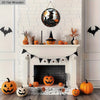 Panneau décoratif d'Halloween avec un chat noir et une sorcière sur une plaque en bois ronde, exposé sur une cheminée en briq
