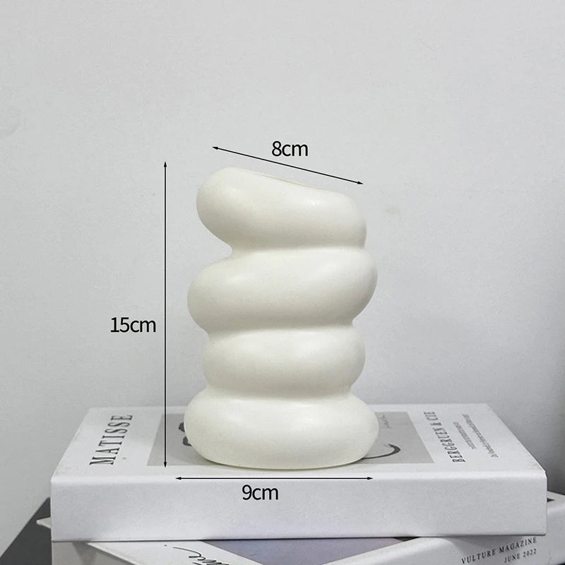 A white, textured plastic decorative vase with a serpentine shape is shown next to a measuring scale.