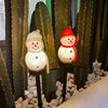 A festive outdoor display featuring three solar-powered Christmas snowman lights in a desert garden setting.