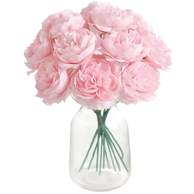 A bouquet of six pink artificial peony flowers in a clear glass vase.