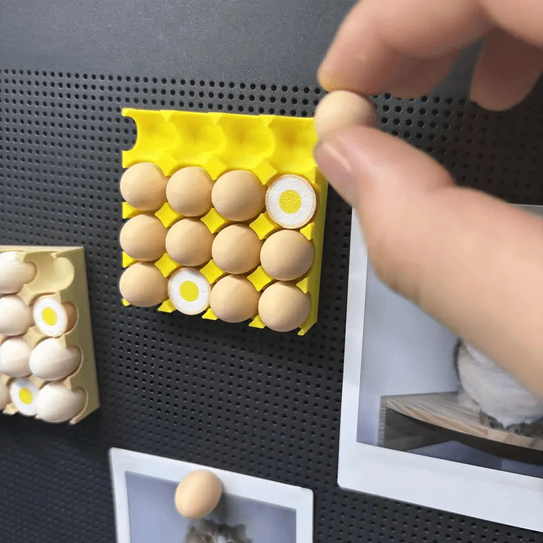 A hand is placing a tan egg onto a yellow magnetic tray filled with other eggs.